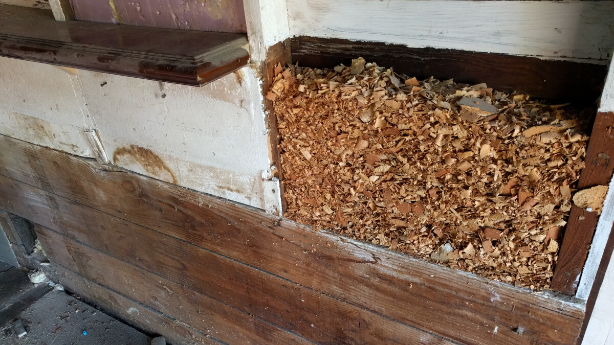 A removed wall panel with wood shaving insulation behind it